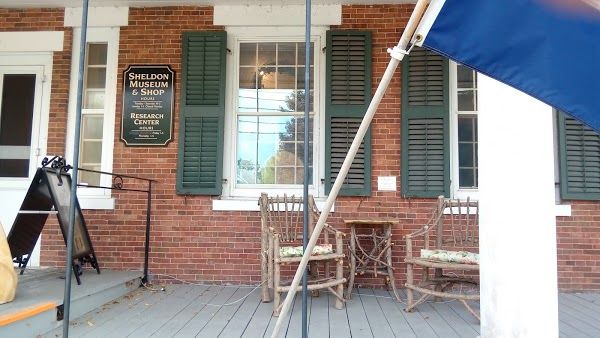 The porch and front entrance to the museum show a flag and a sign with a few chairs to sit in.