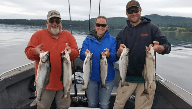 Three people hold up fish while standing on a boat in a lake.